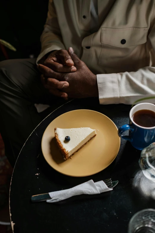 a man sitting at a table with a piece of cake on a plate, a still life, inspired by Barthélemy Menn, trending on unsplash, white + blue + gold + black, coffee shop, ignant, close together