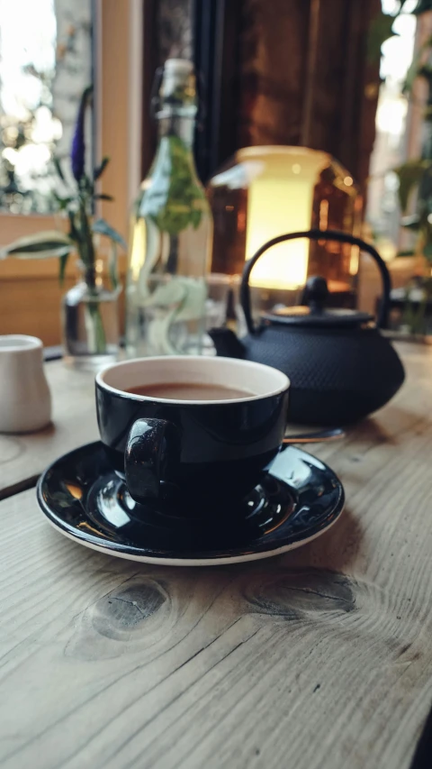 a cup of coffee sitting on top of a wooden table, large black kettle on hearth, in a bright cafe, press shot, thumbnail