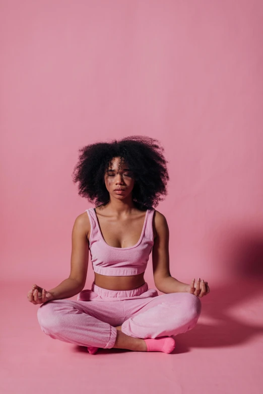 a woman sitting in the middle of a yoga pose, by Lily Delissa Joseph, trending on pexels, renaissance, pink clothes, natural hair, pastel pink neon, calm face