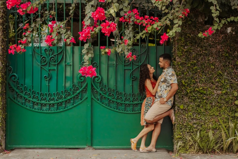 a man and woman standing in front of a green gate, pexels contest winner, bougainvillea, buenos aires, leaning on door, thumbnail