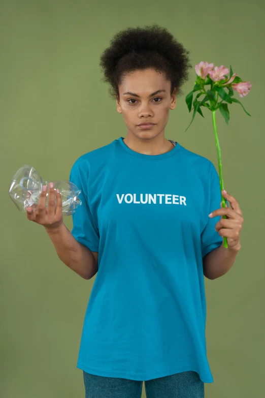 a woman holding a flower in one hand and a plastic bottle in the other, an album cover, inspired by Elke Vogelsang, pexels contest winner, blue tight tshirt, portrait of vanessa morgan, sustainability, - 12p