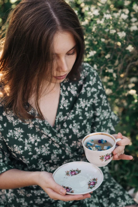 a woman in a floral dress holding a cup and saucer, a portrait, trending on unsplash, pondering, green tea, long coffee brown hair, al fresco