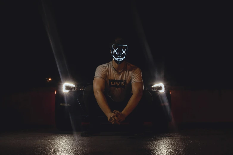 a man sitting in front of a car wearing a neon mask, an album cover, pexels contest winner, scary lighting, anon 5 0 mm, discord profile picture, cross-eyed