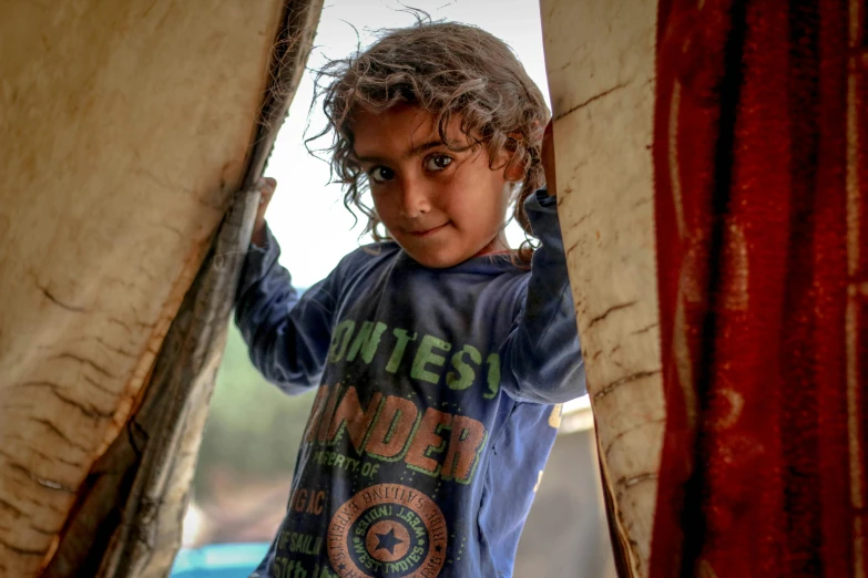 a little boy that is standing in a doorway, by Daniel Lieske, pexels contest winner, hurufiyya, in a colorful tent, portrait of bedouin d&d, his hair is messy and unkempt, cardboard