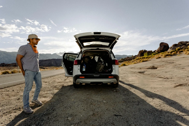 a man standing next to a car on a dirt road, by Jeffrey Smith, unsplash, avatar image, death valley, massive wide trunk, with a roof rack