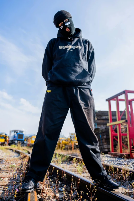 a man in a gas mask standing on a train track, a portrait, unsplash, black and yellow tracksuit, wearing jeans and a black hoodie, wearing farm clothes, on display