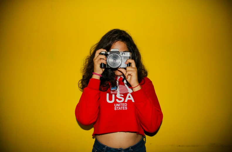 a woman taking a picture with a camera, inspired by Elsa Bleda, pexels contest winner, pop art, red shirt, usa, wearing yellow croptop, usa-sep 20