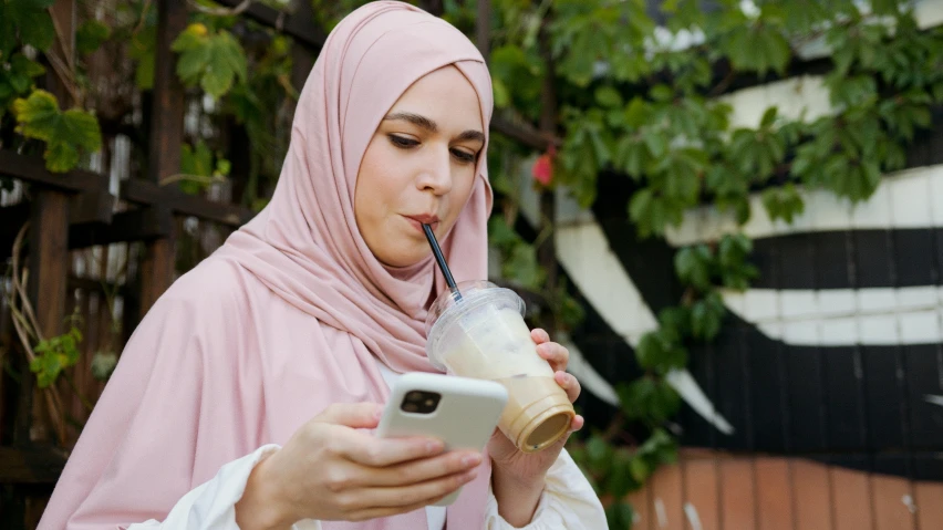 a woman in a hijab is using a cell phone, inspired by Maryam Hashemi, shutterstock, drink milkshakes together, tan, real trending on instagram image, mobile game