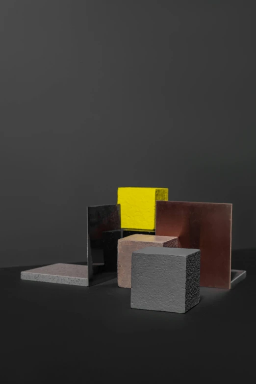 a group of different colored blocks sitting on top of a table, an abstract sculpture, charcoal and yellow leather, dark matte metal, rick owens, on clear background