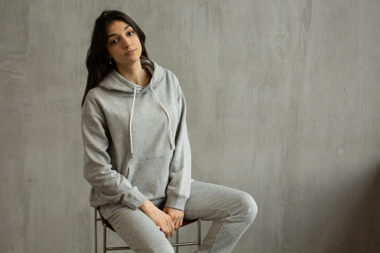 a woman sitting on a chair wearing a hoodie, grey mist, wearing a hoodie and sweatpants, background image, environmental shot