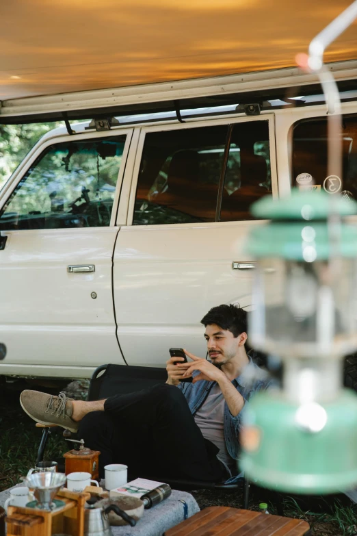 a man sitting under a tent looking at his cell phone, trending on unsplash, renaissance, land rover defender 110 (1985), kombi, hanging out with orbs, australian