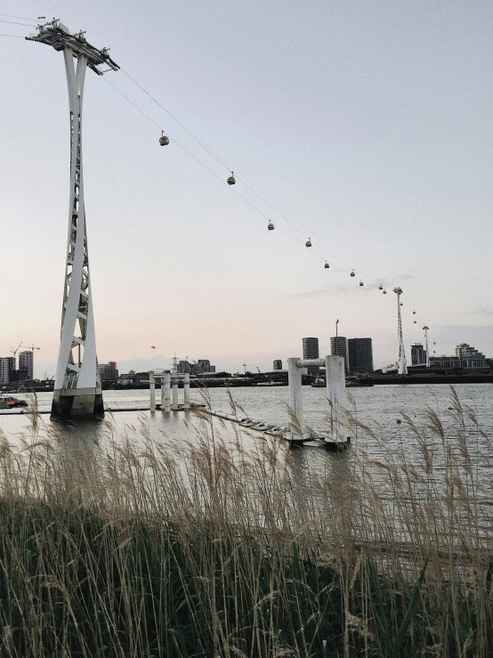 a cable car going over a body of water, by Jacob Toorenvliet, grass field surrounding the city, at dusk!, connected with hanging bridge!!, trending on vsco