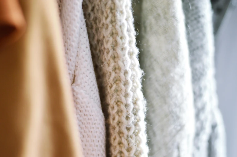 a row of sweaters hanging on a rack, trending on pexels, soft textures, pale colors, upclose, intricate textures