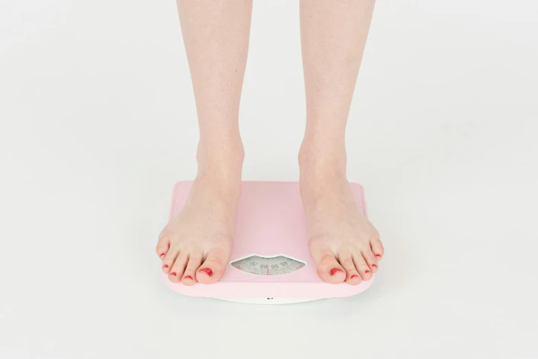 a woman standing on a scale with her feet on it, an album cover, pexels, pastel pink skin tone, in 2 0 1 5, very pale, ready to eat