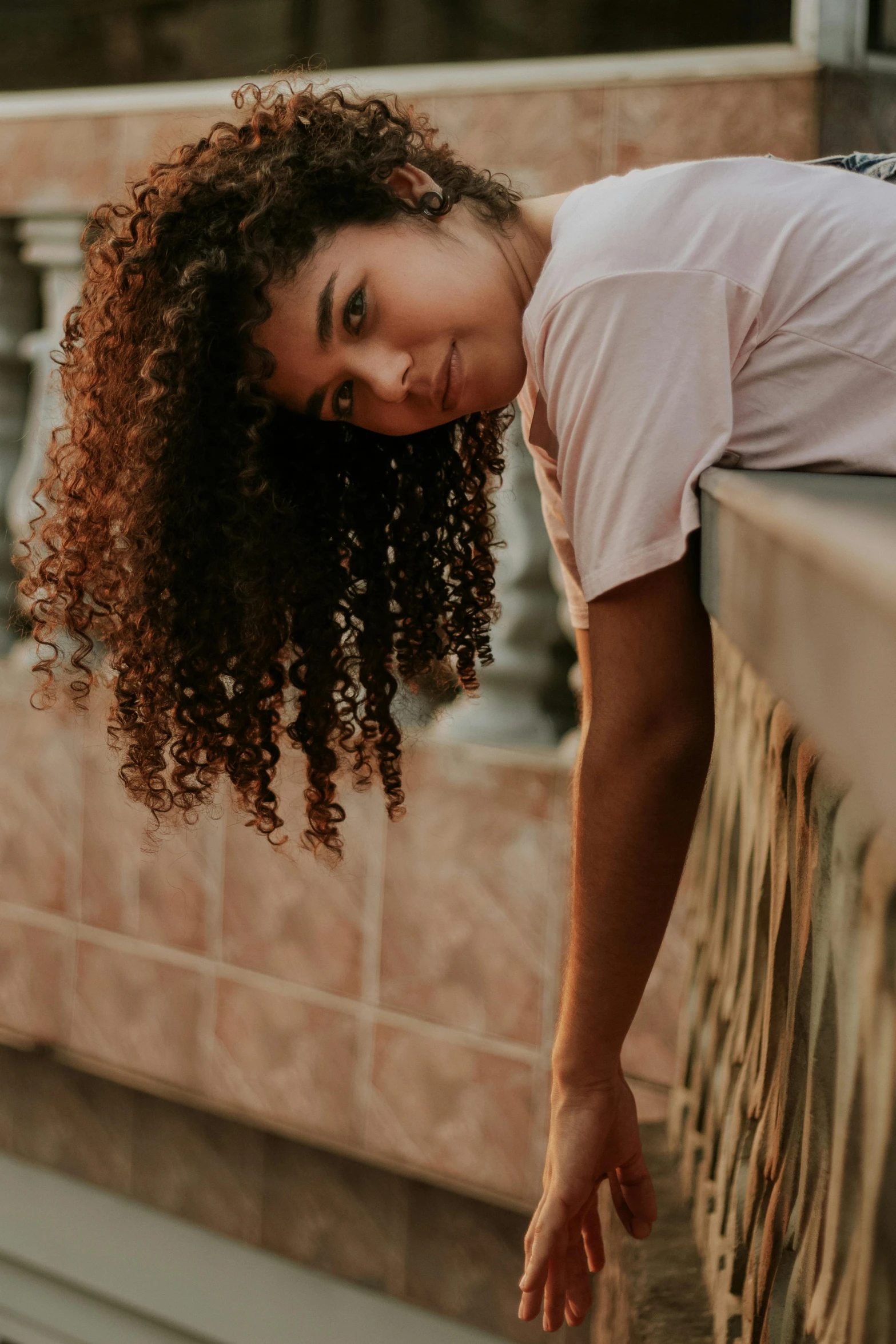 a woman with curly hair leaning on a railing, pexels contest winner, light-brown skin, dressed in a white t shirt, center of image, large)}]