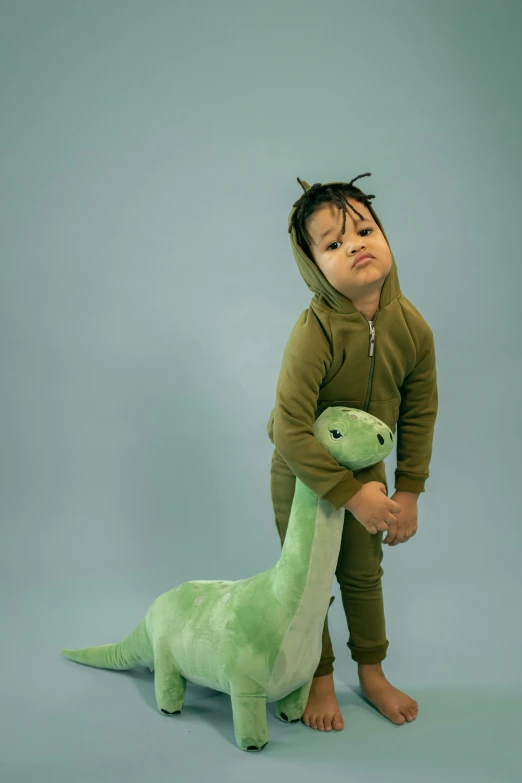 a small child standing next to a stuffed dinosaur, an album cover, inspired by Abidin Dino, trending on pexels, tracksuit, studio photoshot, olive, brachiosaurus