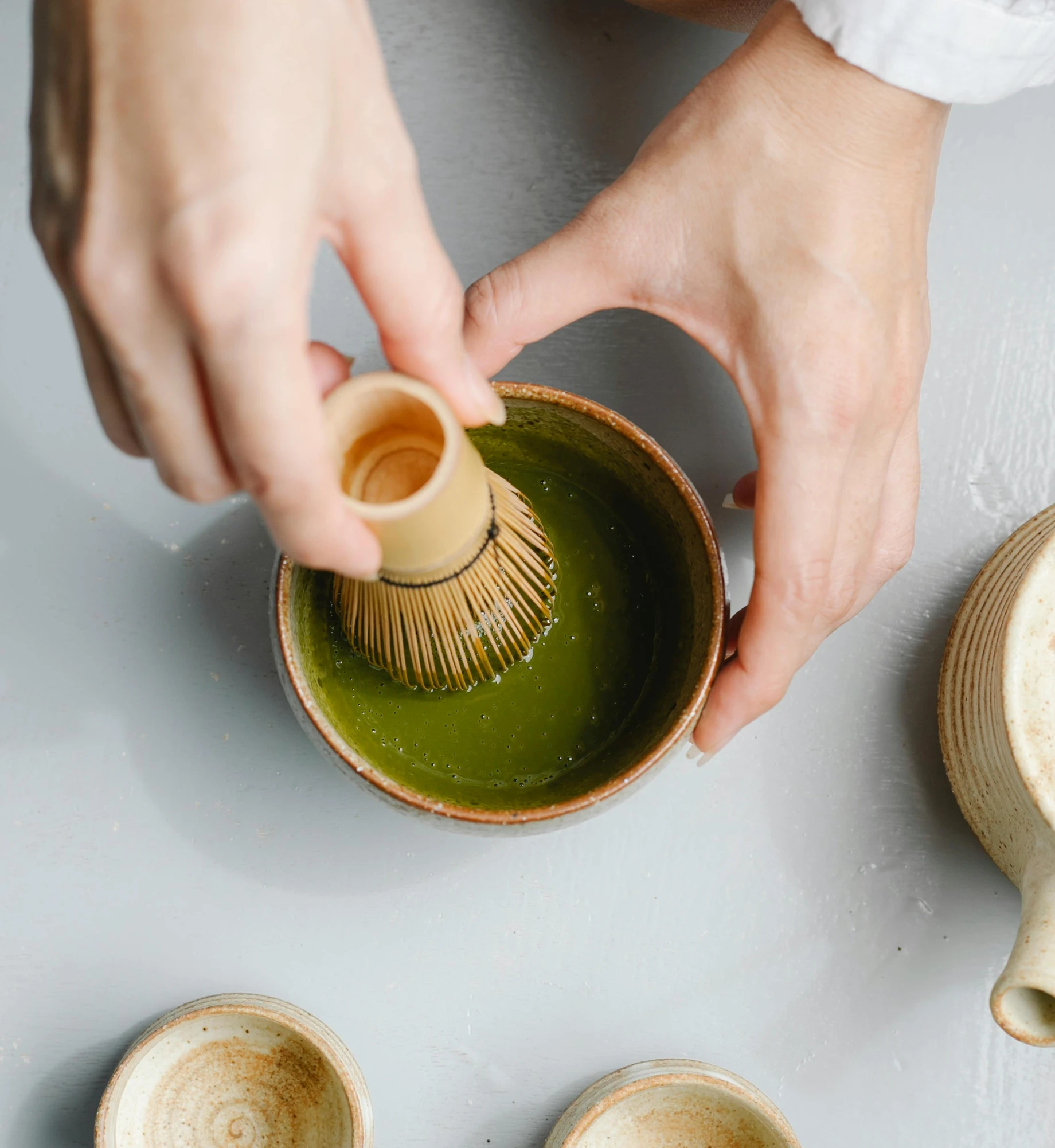 a person holding a whisk over a bowl of green tea, inspired by Kanō Shōsenin, terracotta, creating a soft