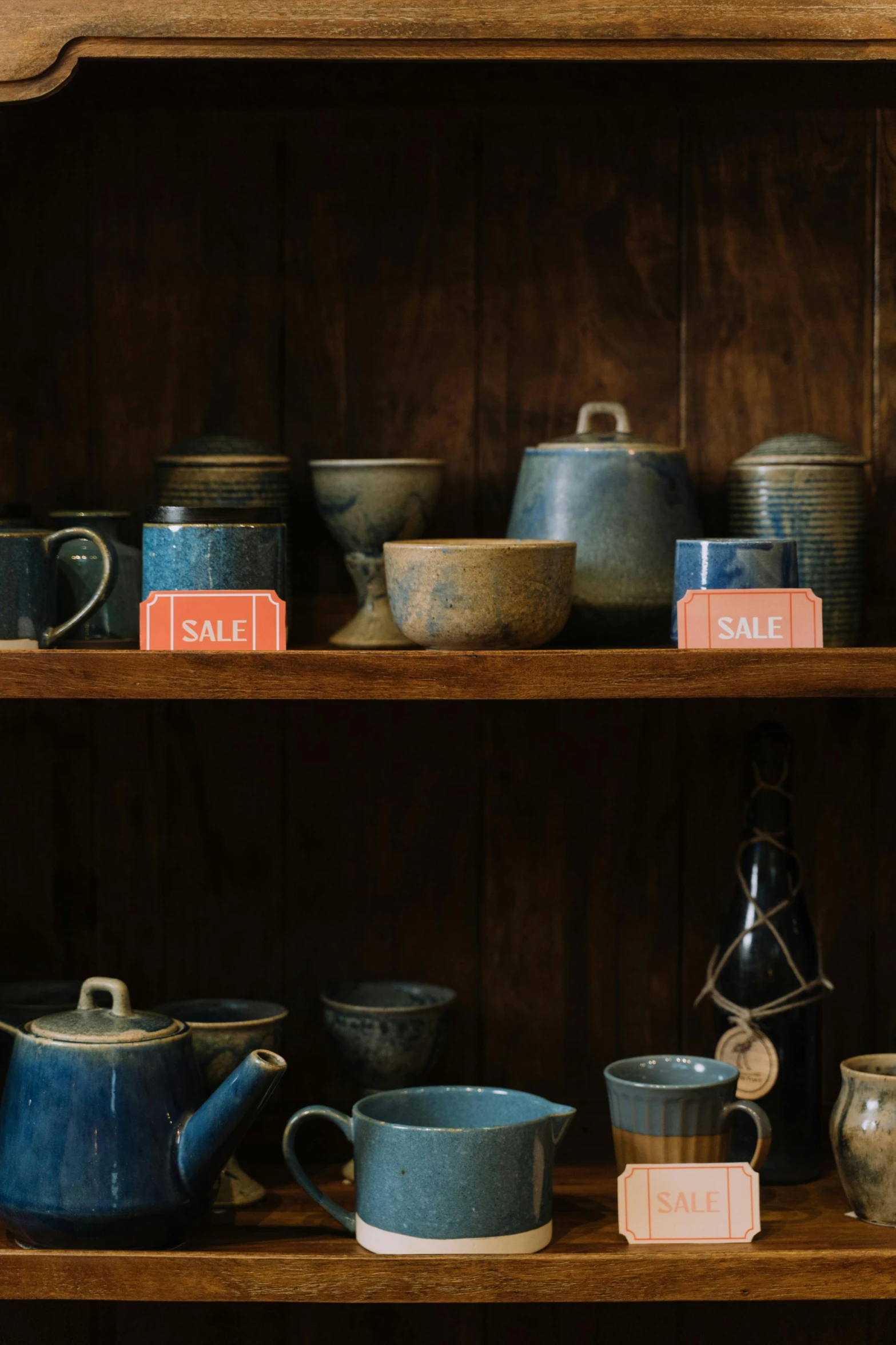 a wooden shelf filled with lots of different types of pottery, by Jessie Algie, trending on unsplash, dark blue, made of glazed, advertising photo, hazy