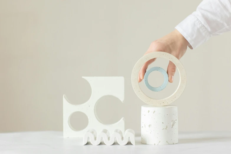 a person holding a roll of tape next to a stack of toilet paper, an abstract sculpture, inspired by Rachel Whiteread, trending on unsplash, new sculpture, white stone arches, white and pale blue toned, textured base ; product photos, circle