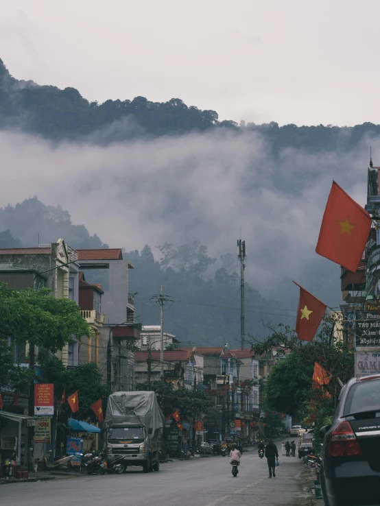 a city street with mountains in the background, pexels contest winner, happening, gang flags, vietnamese temple scene, under a gray foggy sky, profile image