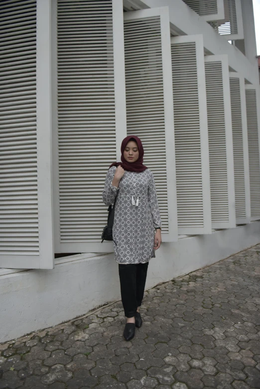 a woman standing in front of a white building, inspired by Naza, hurufiyya, simple clothing!!!!!, patterned, shades of grey, low quality photo