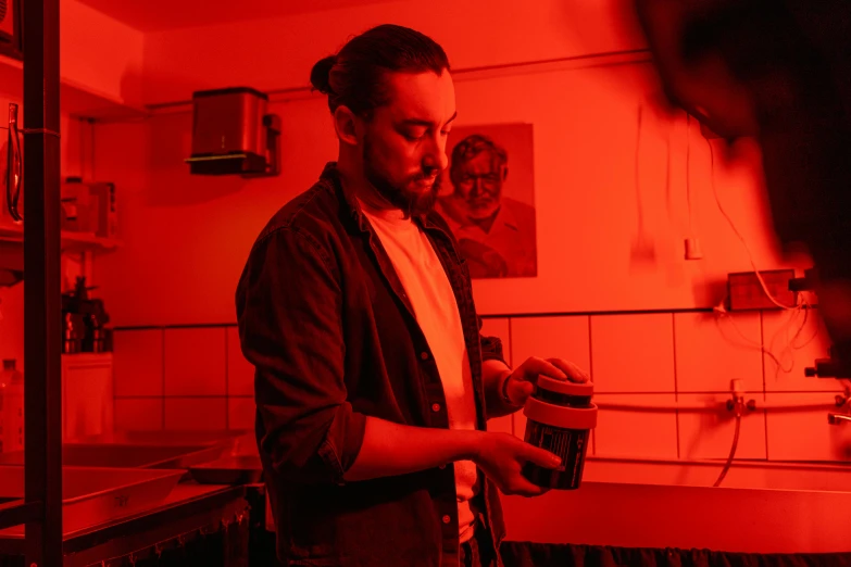 a man standing in a kitchen holding a cup of coffee, by Daniel Lieske, pexels contest winner, process art, red neon light, holding a tin can, aussie baristas, red room