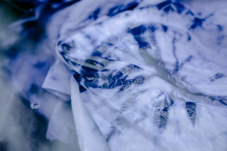 a blue and white shirt sitting on top of a table, inspired by Anna Füssli, unsplash, lyrical abstraction, swirling fabric, extreme close shot, spirits covered in drapery, fractal blue leaves