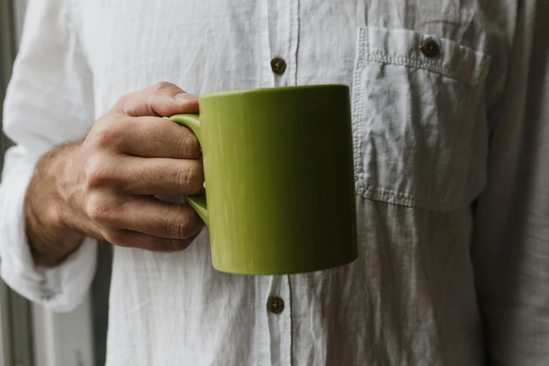 a close up of a person holding a cup, inspired by Lewis Henry Meakin, pexels contest winner, casual green clothing, wearing a linen shirt, white mug, lime green