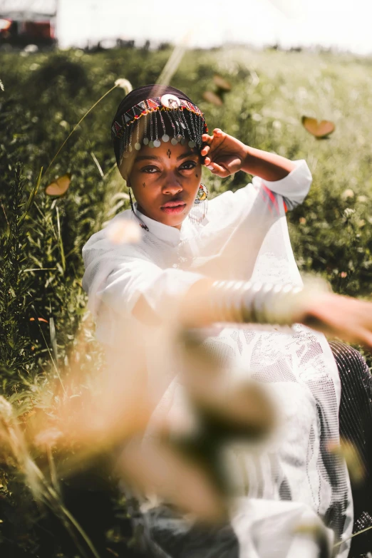 a woman sitting on top of a lush green field, an album cover, inspired by Makoto Aida, unsplash, afrofuturism, white sleeves, gold wings on head, portrait willow smith, medium format. soft light