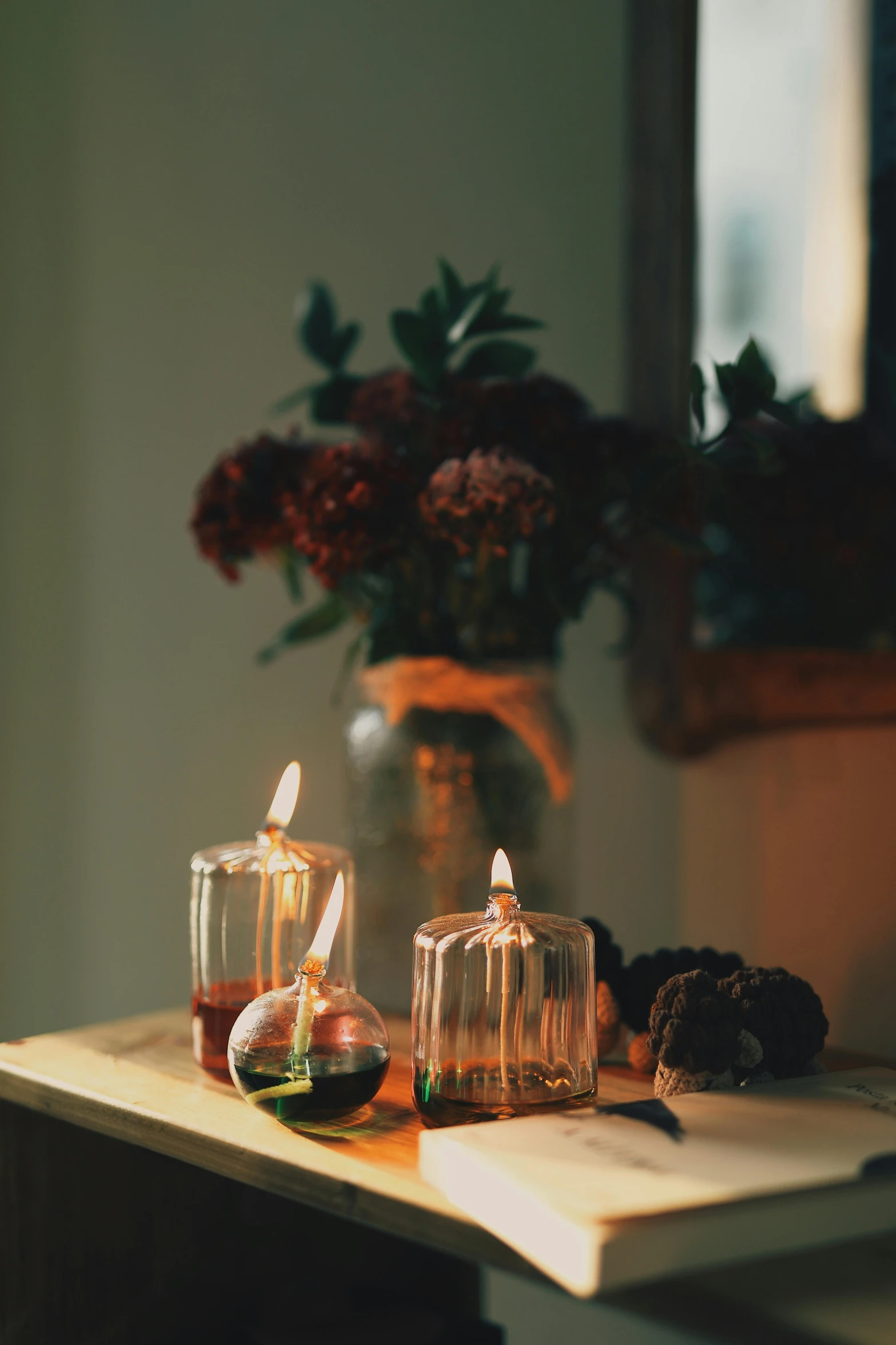 a candle sitting on top of a table next to a vase of flowers, glass domes, autumnal colours, perfume, fire lit