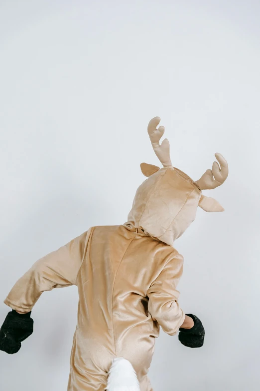 a person dressed up in a reindeer costume, by Nina Hamnett, trending on pexels, plain background, little kid, back - shot, tan suit