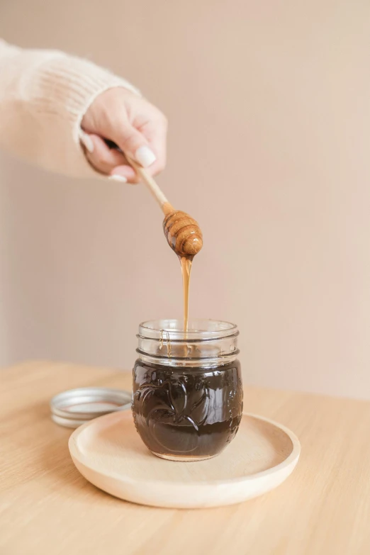 a person dipping honey into a jar on a plate, sitting on a mocha-colored table, black resin, organic color, thumbnail