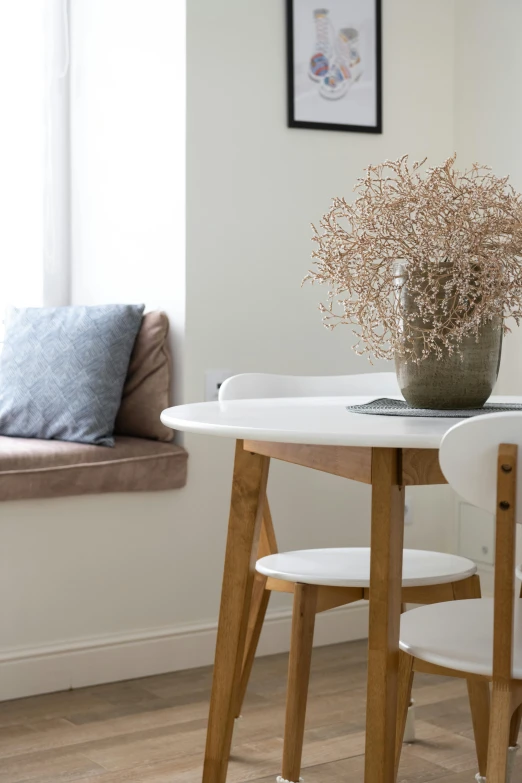 a white table with a vase of flowers on top of it, inspired by Constantin Hansen, unsplash, minimalism, brown and cream color scheme, city apartment cozy calm, tables and chairs, detail shot