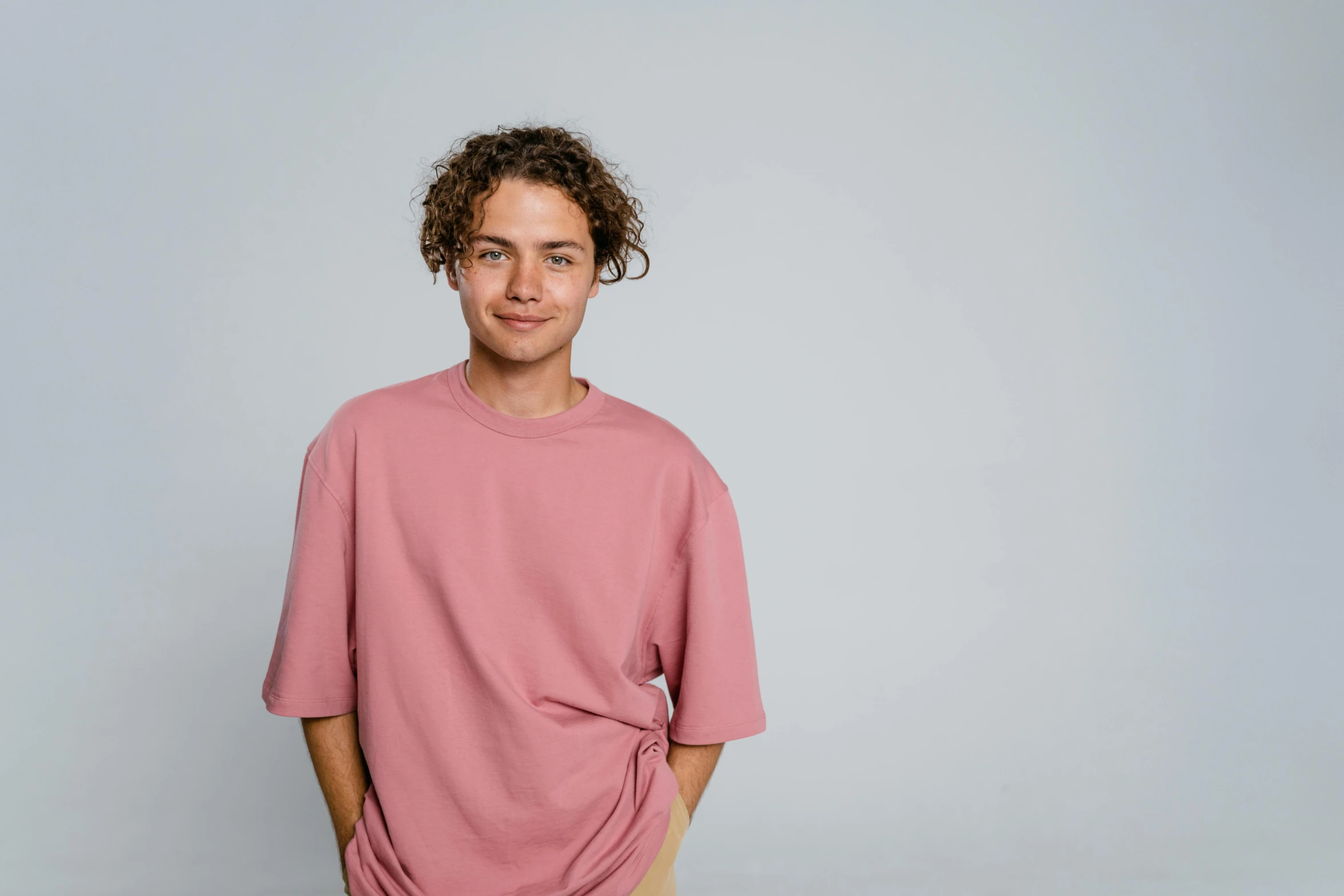 a young man standing with his hands in his pockets, a character portrait, pexels contest winner, happening, pink shirt, he has short curly brown hair, productphoto, teenage girl