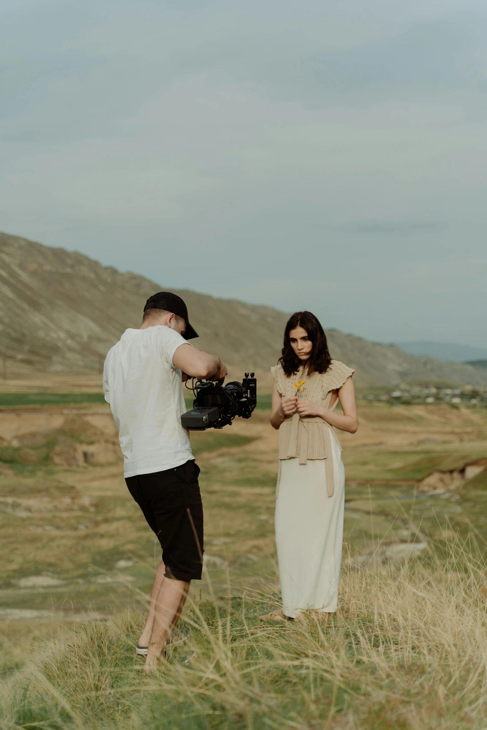 a man standing next to a woman in a field, pexels contest winner, video art, holding a camera, hills in the background, cinematic mid shot fight, studio photo