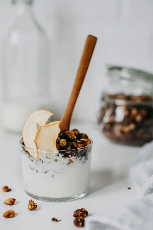 a glass of yogurt with a cinnamon stick sticking out of it, by Nicolette Macnamara, trending on pexels, cereal, pear, jars, grey