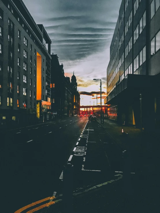 a city street filled with lots of tall buildings, an album cover, inspired by Elsa Bleda, pexels contest winner, realism, glasgow, moody sunset and dramatic sky, dark wet road, vibrant but dreary