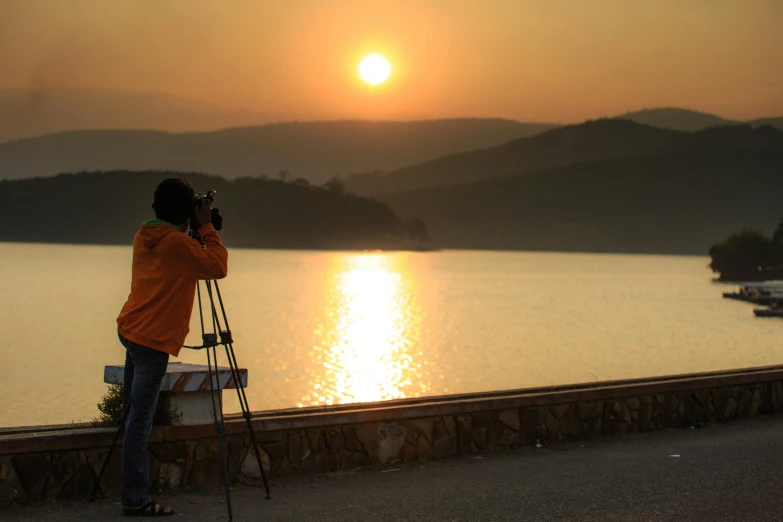 a man taking a picture of the sun setting over a lake, pexels contest winner, art photography, telephoto, today\'s featured photograph 4k, tripod, street photo