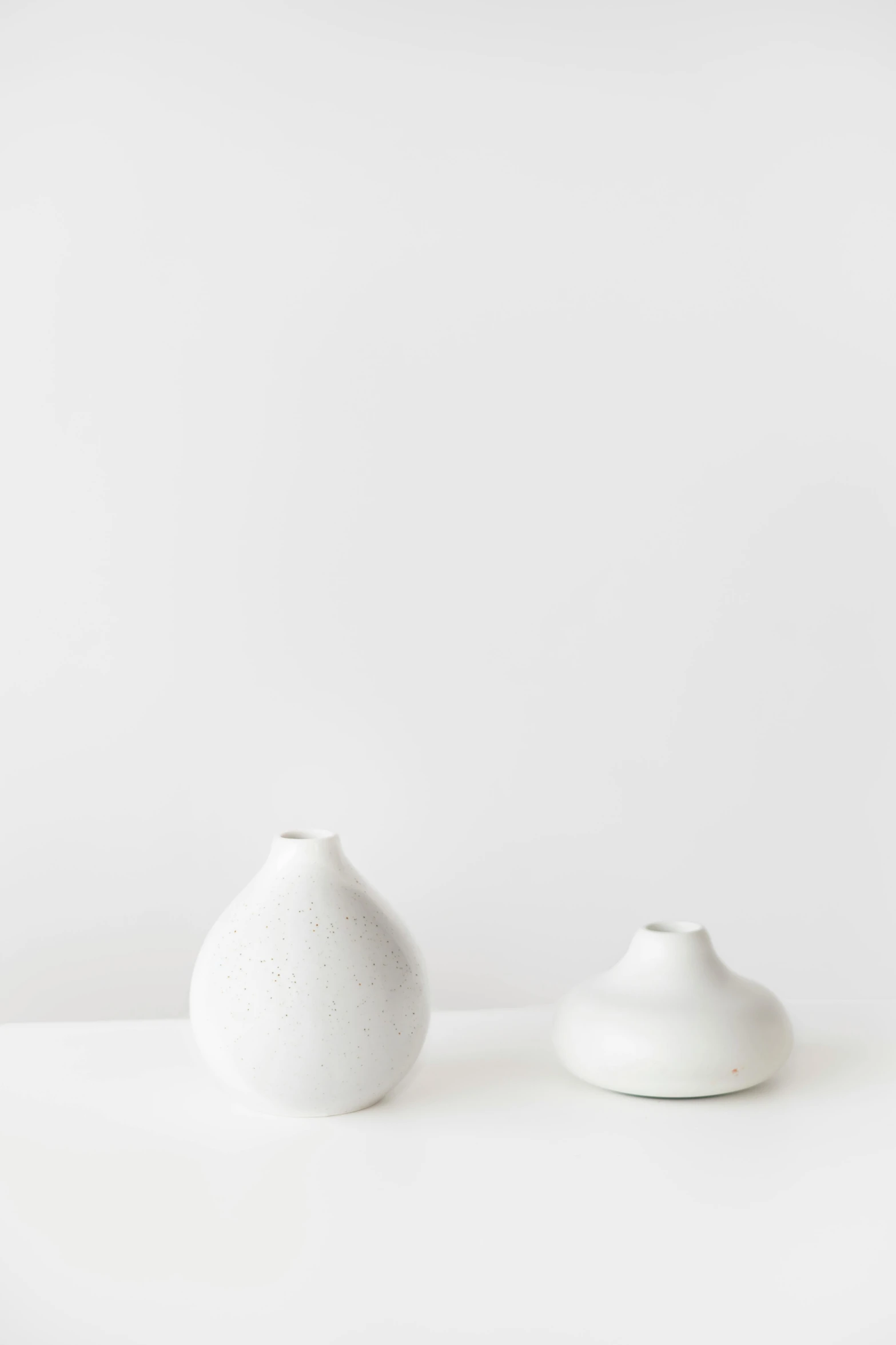 a couple of white vases sitting on top of a table, unsplash, minimalism, matte white background, made of silk paper, round bottle, h 576