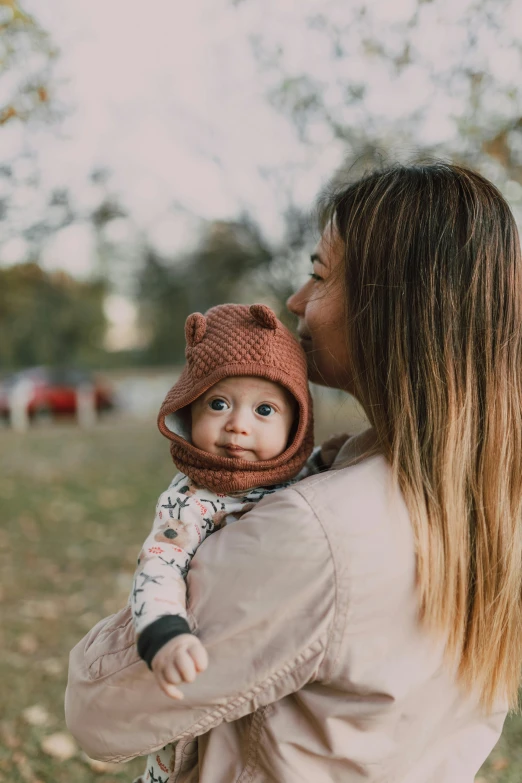 a woman holding a baby in her arms, pexels contest winner, hat and hoodie, square, brown hat, bears