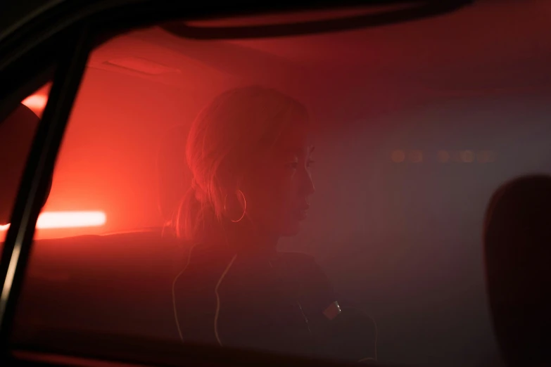 a woman sitting in the passenger seat of a car, inspired by Elsa Bleda, small red lights, ambient amber light, haze, standing in a dimly lit room