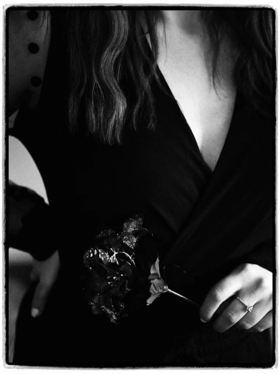 a black and white photo of a woman holding a flower, a black and white photo, by Lucia Peka, black dress with belt, shot with iphone 1 0, medium format. soft light, robe. extremely high details