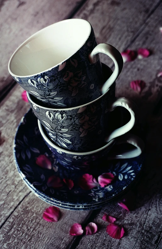 a couple of cups sitting on top of a wooden table, a still life, inspired by Isabel Codrington, unsplash, floral pattern, dark colour scheme, hero shot, vintage photograph