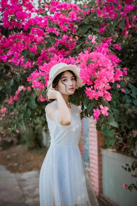 a woman standing in front of a bush of pink flowers, pexels contest winner, aestheticism, white hat, young asian girl, wearing in a summer dress, girl cute-fine-face