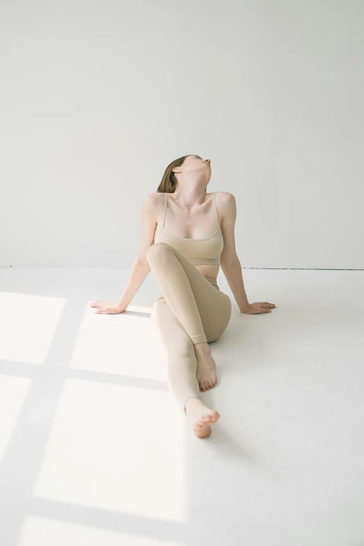 a woman sitting on the floor in a white room, inspired by Fei Danxu, unsplash, muted colored bodysuit, beige, head tilted down, yoga pose