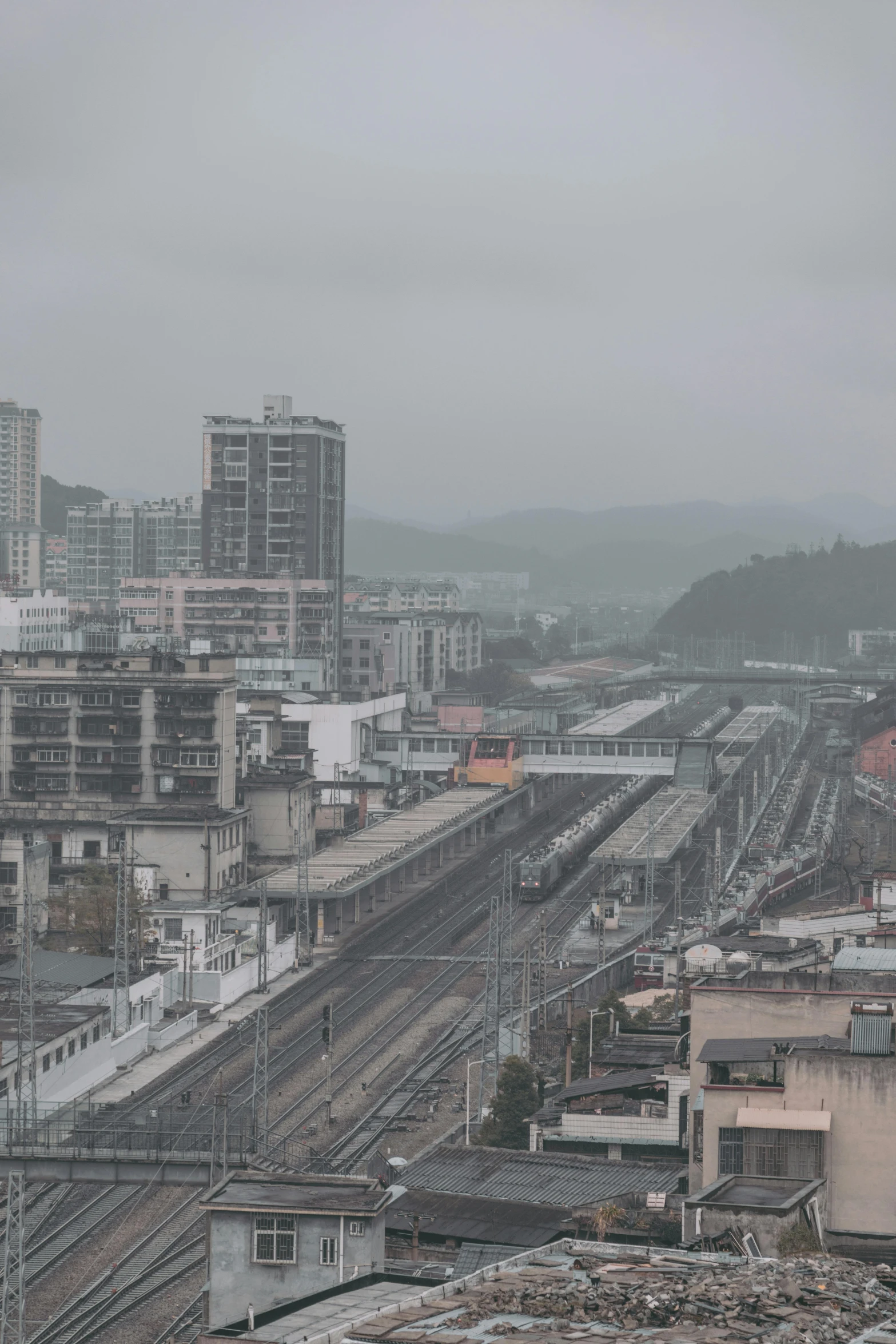 a train traveling through a city next to tall buildings, inspired by Zhang Kechun, unsplash, overcast!!! cinematic focus, small town surrounding, guangjian, square