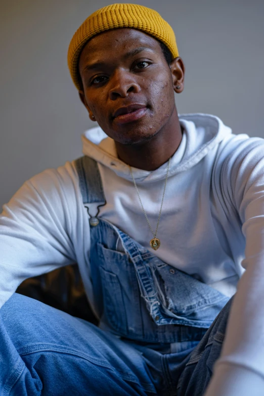 a man sitting on a couch wearing a yellow hat, by Richmond Barthé, trending on pexels, wearing blue jean overalls, non binary model, riyahd cassiem, portrait of thancred