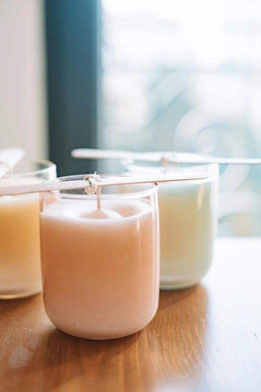 a group of candles sitting on top of a wooden table, pale pastel colours, soymilk, promo image, dwell