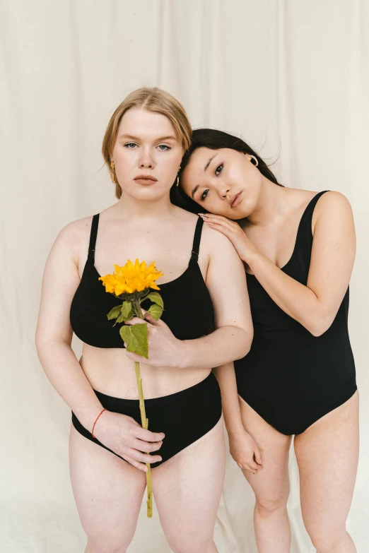 a couple of women standing next to each other, black underwear, holding a flower, curated collection, pale skin!