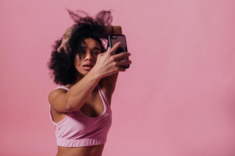 a woman taking a selfie with her cell phone, trending on pexels, happening, pink body, with textured hair and skin, fight pose, mirroring